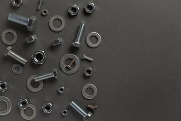 Metal steel chrome shiny nuts and bolts scattered on a grey background