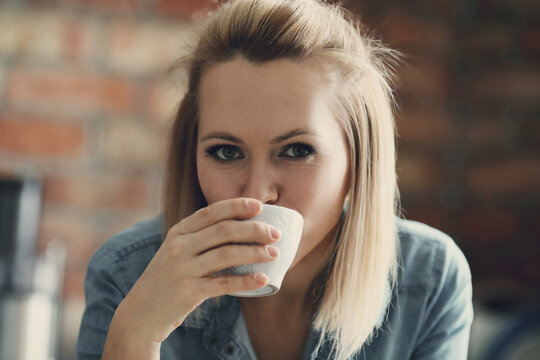 Picture of young blond woman with short hair looking at camera and drinking a cup of tea in the kitchen