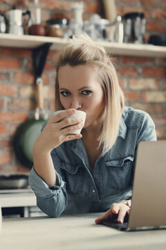 Picture of young blond woman with short hair looking at camera and drinking a cup of tea in the kitchen