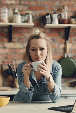 Picture of young blond woman with short hair holding a cup of coffee in the kitchen