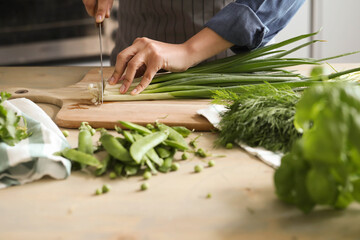 Women’s hands cut fresh green onion salad on the kitchen table