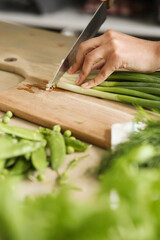 Obraz premium Women’s hands cut fresh green onion salad on the kitchen table