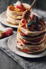 Beautifully decorated delicious sweet pancakes with strawberries and honey on the plate