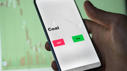 An investor's analyzing the coal etf fund on screen. A phone shows the ETF's prices energy carbon to invest