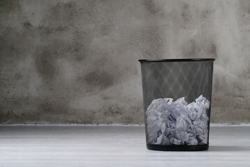 Trash can full of creased white paper balls on a dark background