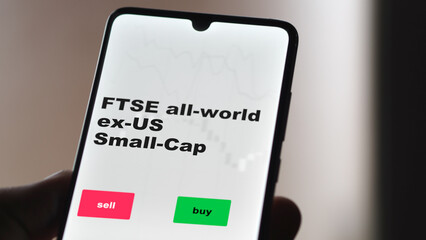 An investor's analyzing the FTSE all-world ex-US Small-Cap etf fund on screen. A phone shows the ETF's prices ftse London all-world ex-US Small-Cap to invest