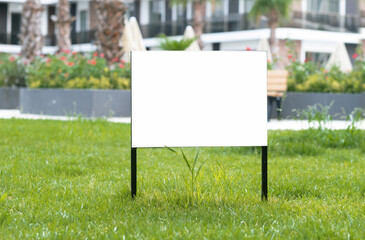 Empty sign, advertising mock-up, banner on grass near pavement in city green park.Copy space for...