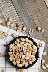 Flat lay of pistachio nuts in dark bowl isolated on a wooden background.