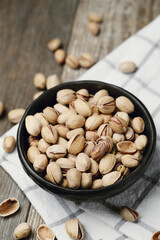 Image of pistachio nuts in dark bowl isolated on a wooden background.