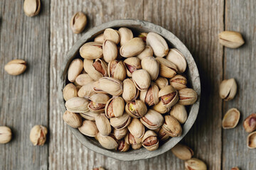 Image of pistachio nuts in gray bowl isolated on a wooden background.