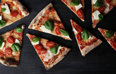 Slices of delicious pizza with cheese, tomato and spinach on a black background