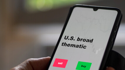 An investor's analyzing the stocks etf fund on screen. A phone shows the ETF's prices U.S. broad thematic to invest