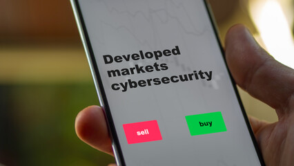 An investor's analyzing the stocks etf fund on screen. A phone shows the ETF's prices developed markets cybersecurity to invest
