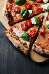 Slices of delicious pizza with cheese, cherry tomatoes and greens on a wooden background