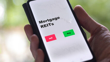 An investor's analyzing the reit on screen. A phone shows the ETF's prices mortgage REITs text in english.