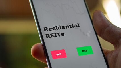 An investor's analyzing the reit on screen. A phone shows the ETF's prices residential REITs