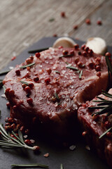 Raw fresh red meat with rosemary and spices on a black board