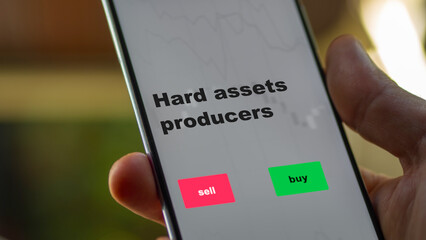 An investor's analyzing the stocks on screen. A phone shows the ETF's prices hard assets producers