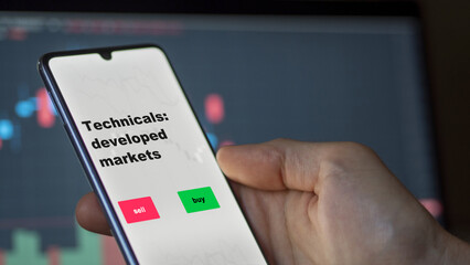 An investor's analyzing the stocks on screen. A phone shows the ETF's prices technicals: developed markets