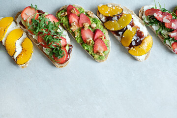 A row of various tasty fresh Bruschetta (sandwiches) with cherry tomatoes, mozzarella cheese and herbs on a white background.