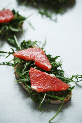 Close view of delicious Bruschetta (sandwiches) with arugula and slices of grapefruit on a white background