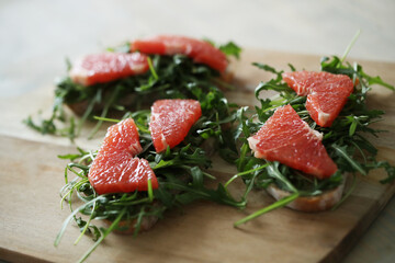 Three yummy sweet Bruschetta (sandwiches) with arugula and slices of grapefruit on a wooden cutting board 