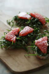 Three yummy sweet Bruschetta (sandwiches) with arugula and slices of grapefruit on a wooden cutting board 