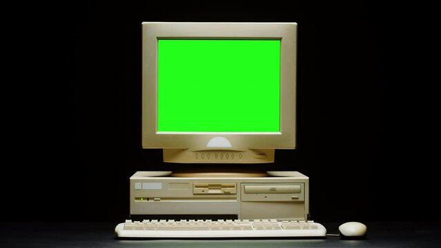 Old computer with green chroma key screen close-up, Desktop PC isolated on black background. Retro obsolete technology. 