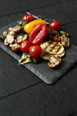 Picture of tasty hot grilled food with various vegeables on a black wooden cutting board