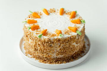 Delicious carrot cake decorated with mastic sweet carrots. Homemade carrot cake with yellow crumbs in the white plate on the white background