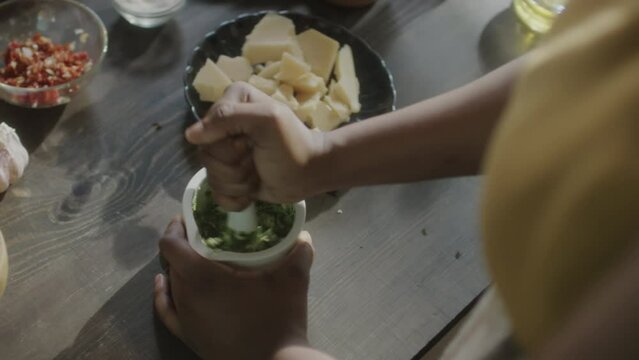 High angle close up shot of African American woman crushing ingredients with mortar and pestle while preparing Pesto sauce