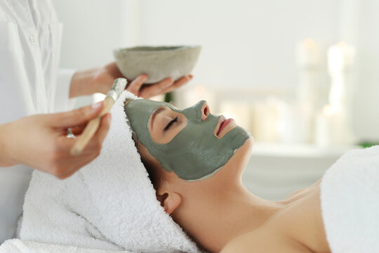 The beautician putting a clay mask on the face of a beautiful young woman in the spa salon
