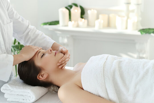 Beautician doing face massage of young beautiful relaxed woman in spa salon
