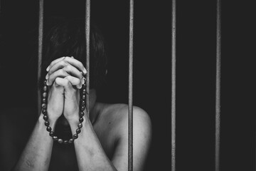 prison male inmate in prison with bead in hand raises his hand to make a wish and pray on black background.concept for prisoner,sadness,detain,erroneousness