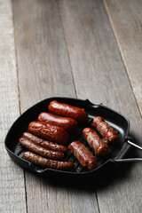 Delicious homemade hot grilled sausage in a black pan on a wooden background