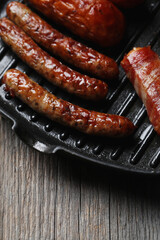 Delicious homemade hot grilled sausage in a black pan on a wooden background