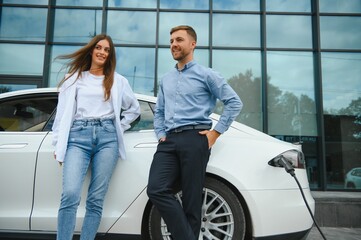 Smiling man and woman on the charging station for electric cars. A man is charging a car.