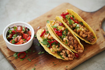 Many different fresh Mexican tacos with meat and vegetable fillings on a wooden cutting board