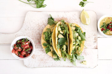 Traditional Mexican tacos with avocado and greens on a white cutting board