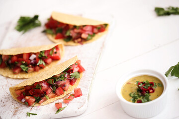 Traditional fresh Mexican tacos with sliced tomatoes and greens on a white cutting board