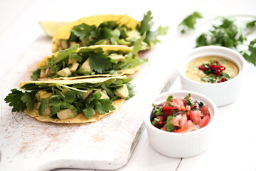 Traditional Mexican tacos with avocado and greens on a white cutting board