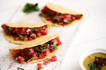 Traditional fresh Mexican tacos with sliced tomatoes and greens on a white cutting board