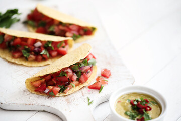 Traditional fresh Mexican tacos with sliced tomatoes and greens on a white cutting board