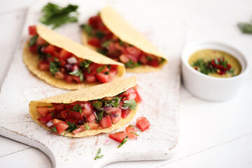 Traditional fresh Mexican tacos with sliced tomatoes and greens on a white cutting board