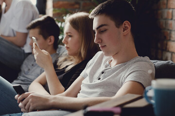 Four teenagers have fun with smartphones on the couch at home