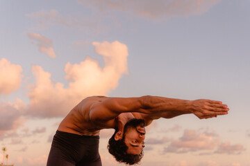 Young beautiful man practicing ashtanga yoga at sunset on the beach. Doing exercises and...