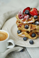 Belgian waffles with blueberries, raspberries , strawberries and powdered sugar on a white plate .