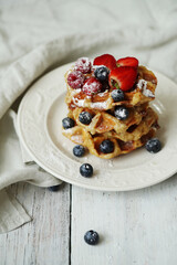 Belgian waffles with blueberries, raspberries , strawberries and powdered sugar on a white plate .