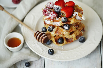 Belgian waffles with blueberries, raspberries , strawberries and powdered sugar on a white plate .