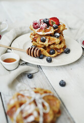 Belgian waffles with blueberries, raspberries , strawberries and powdered sugar on a white plate .